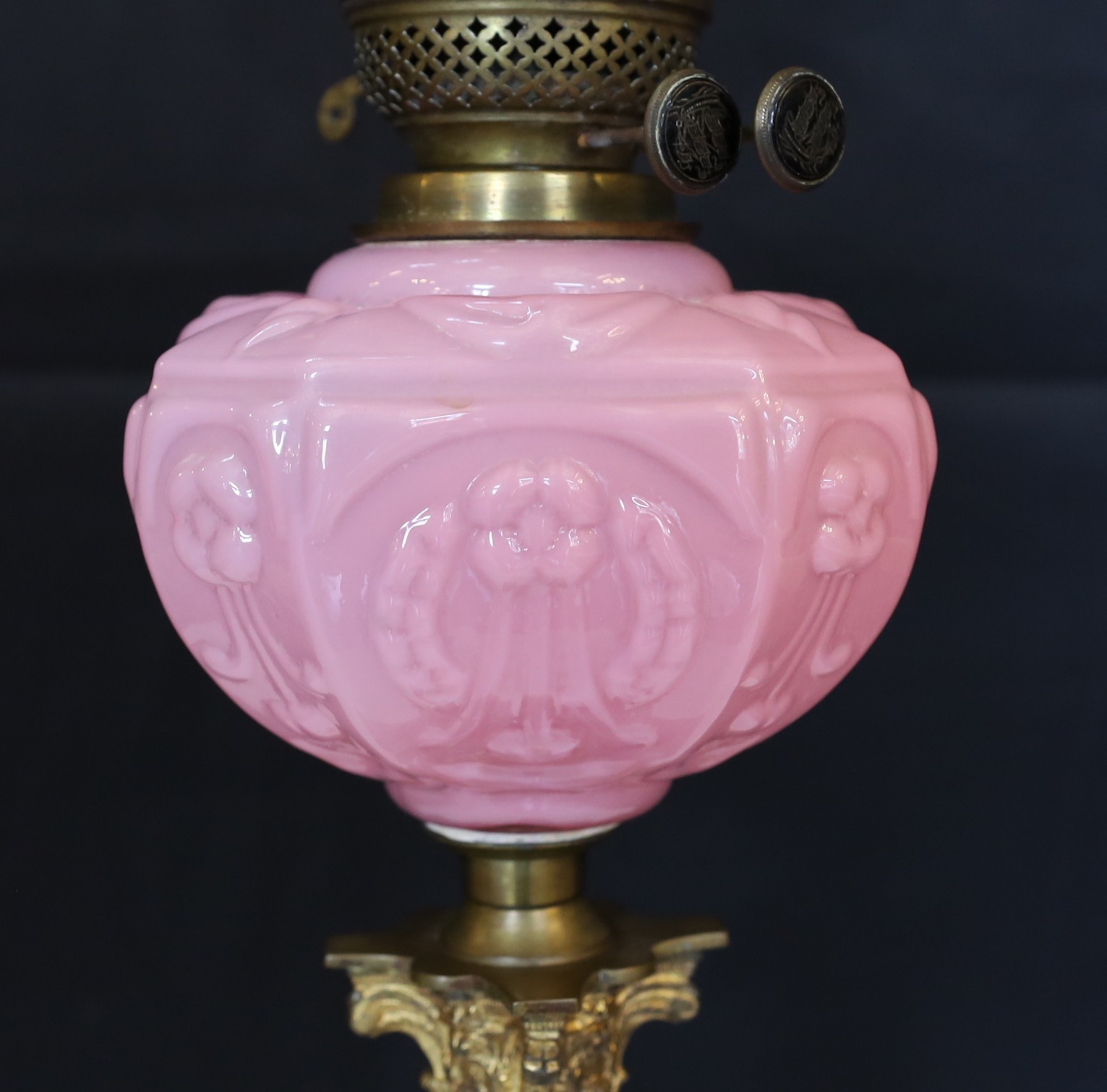 An Edwardian brass Corinthian column oil lamp with opaque pink glass reservoir, etched glass globe and flue, height overall 80cm